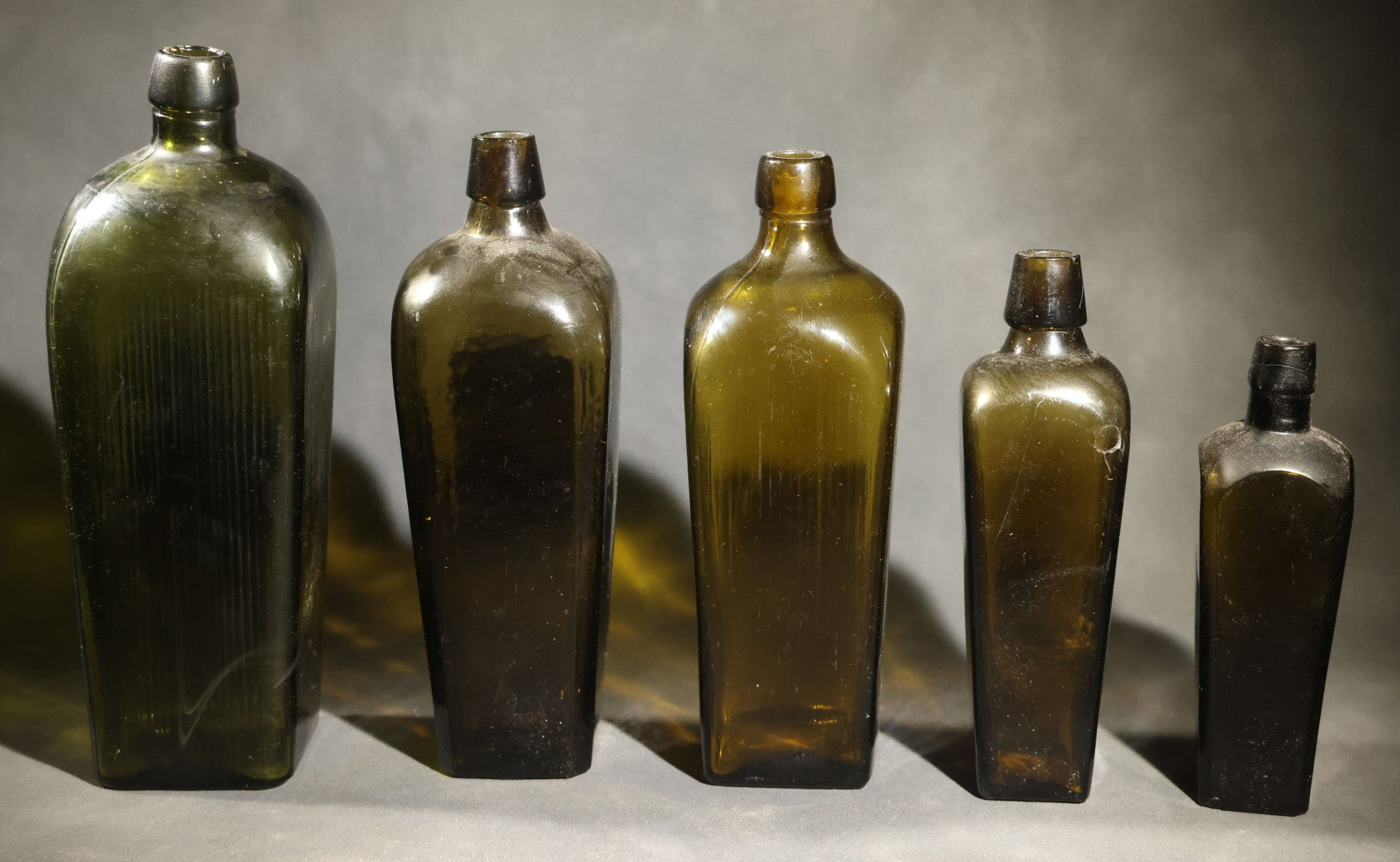 Grouping of Five Antique Case Bottles, Olive Green and Amber Glass, Tapered Square Form, Possible Gin Bottles, 19th Century & 20th century