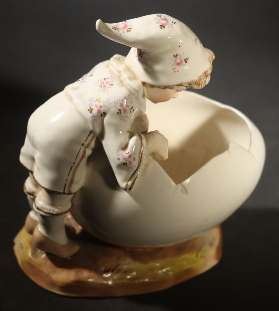 Antique Porcelain Figurine of Child in Stocking Cap Looking into Large Egg, Manufactured by Gebruder Heubach, Lichten, Germany, Note Chip