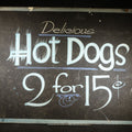 Lot 036 - Vintage Hand-Lettered Paperboard Hot Dog Stand Sign "Delicious Hot Dogs 2 for 15¢" With White and Blue Paint on Black Background, 14-3/8" W x 11-1/8" H