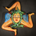 Lot 058 - Vintage Cast Metal Sicilian Trinacria with Polychrome Painted Medusa Head, Green Serpent Hair, Blue Wings, and Three Orange Legs in Triskelion Formation, 7-3/8" L x 8-5/8" H
