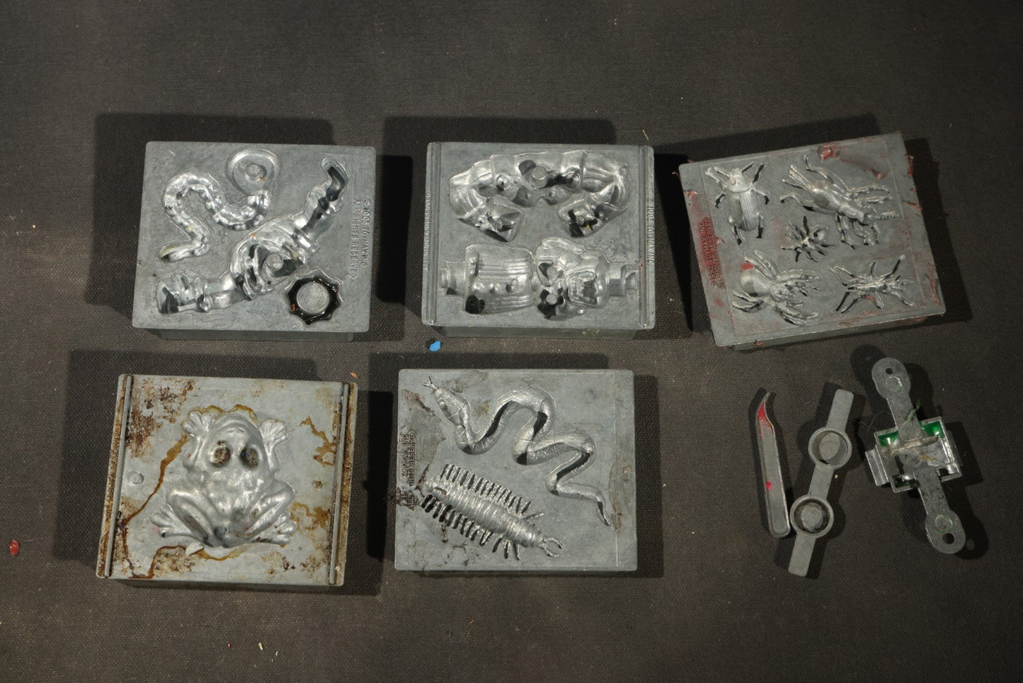Grouping of 47 Vintage Creepy Crawler Metal Molds including Spiders, Skulls, Insects, and Monsters, Mostly Copyright 1994 by Toymax, with Purple Plastic Toymax Carrying Case