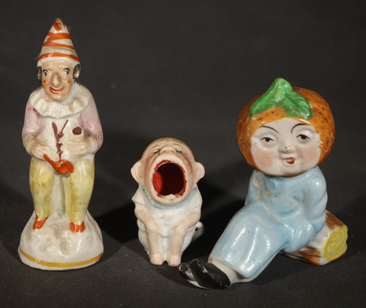 Trio of Vintage Porcelain Figurines including Clown with Violin, Open-Mouth Yawning Baby, and Orange-Head Child on Log