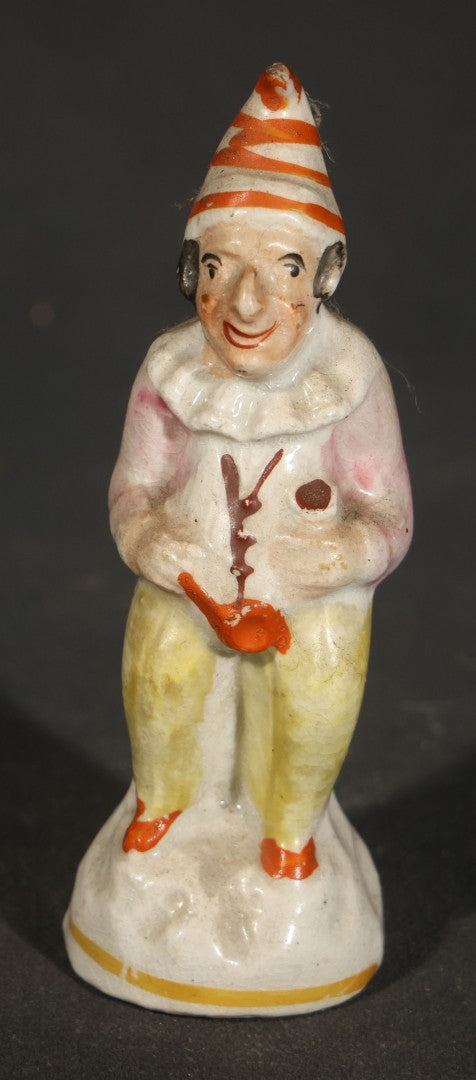 Trio of Vintage Porcelain Figurines including Clown with Violin, Open-Mouth Yawning Baby, and Orange-Head Child on Log