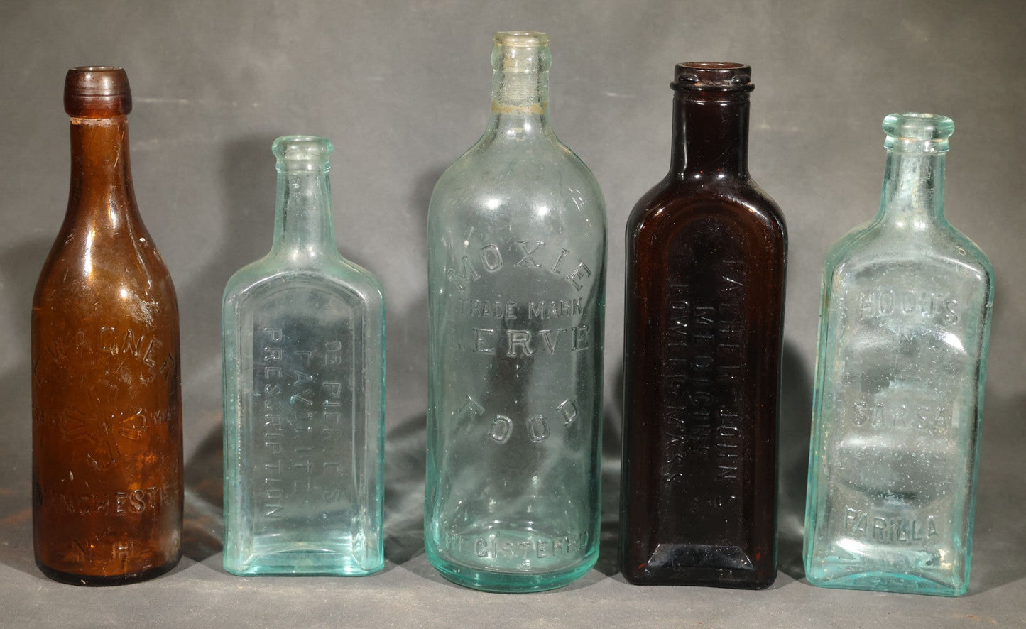 Grouping of Five Antique Embossed Glass Bottles including Moxie Nerve Food, Father John's Medicine, and Hood's Sarsaparilla