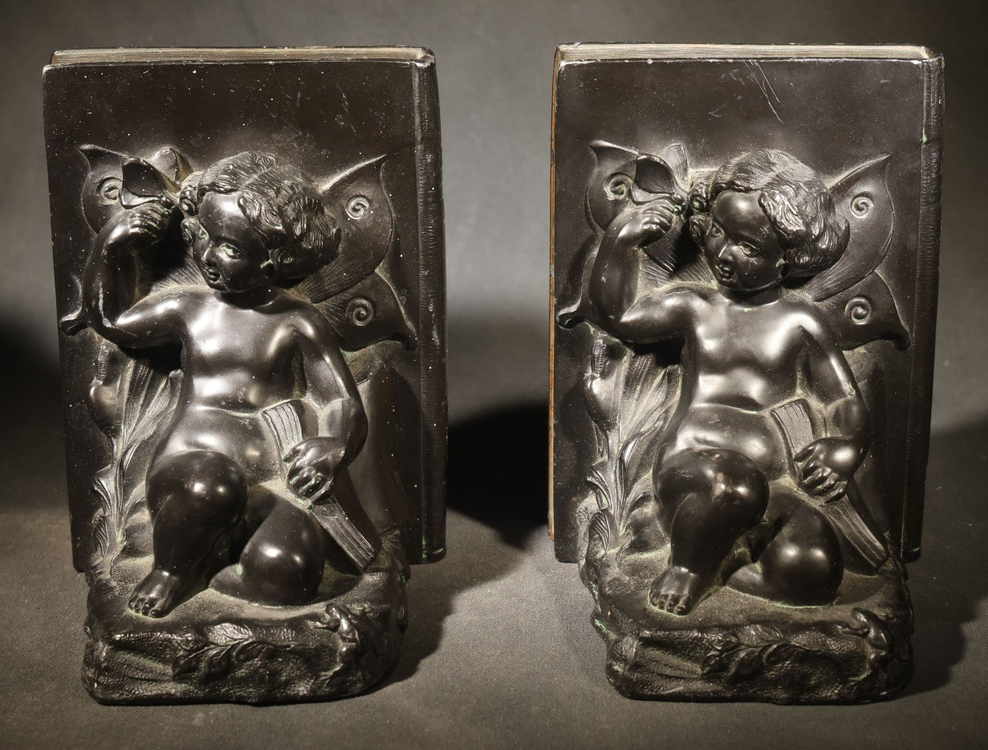 Pair of Antique Figural Bookends with Butterfly-Winged Child Seated Against Book-Form Back