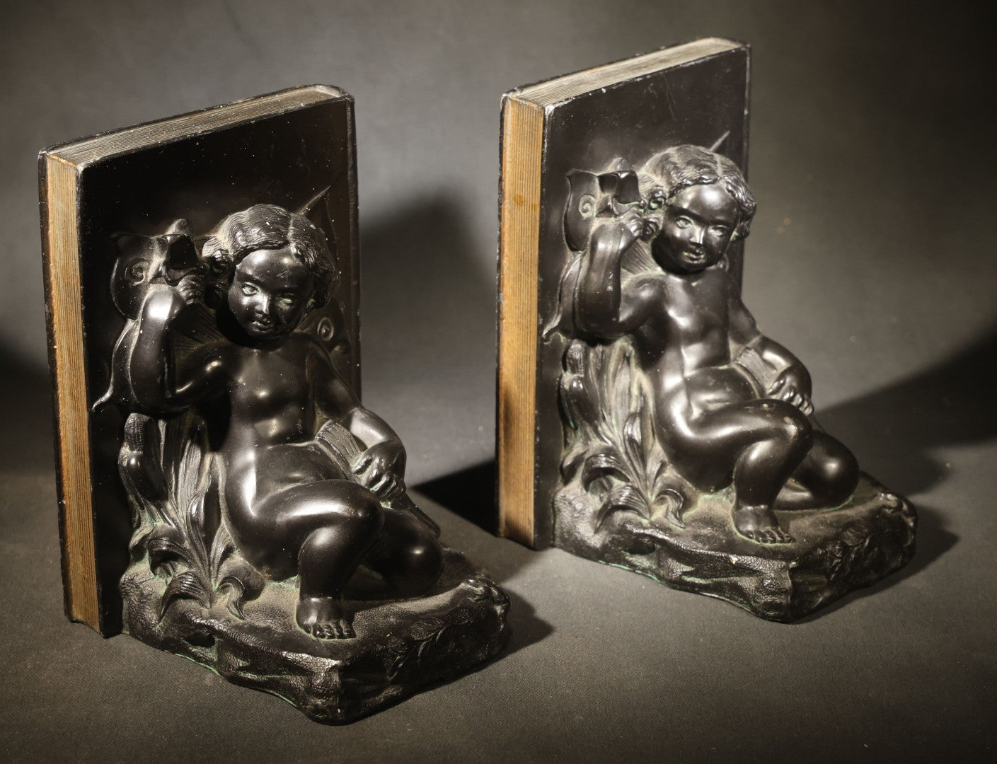 Pair of Antique Figural Bookends with Butterfly-Winged Child Seated Against Book-Form Back
