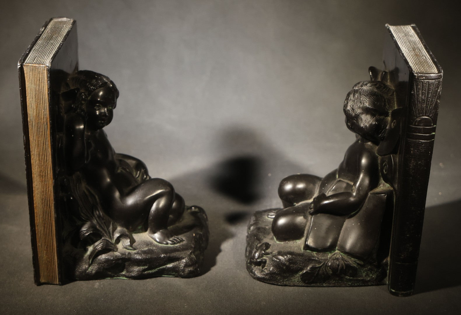 Pair of Antique Figural Bookends with Butterfly-Winged Child Seated Against Book-Form Back