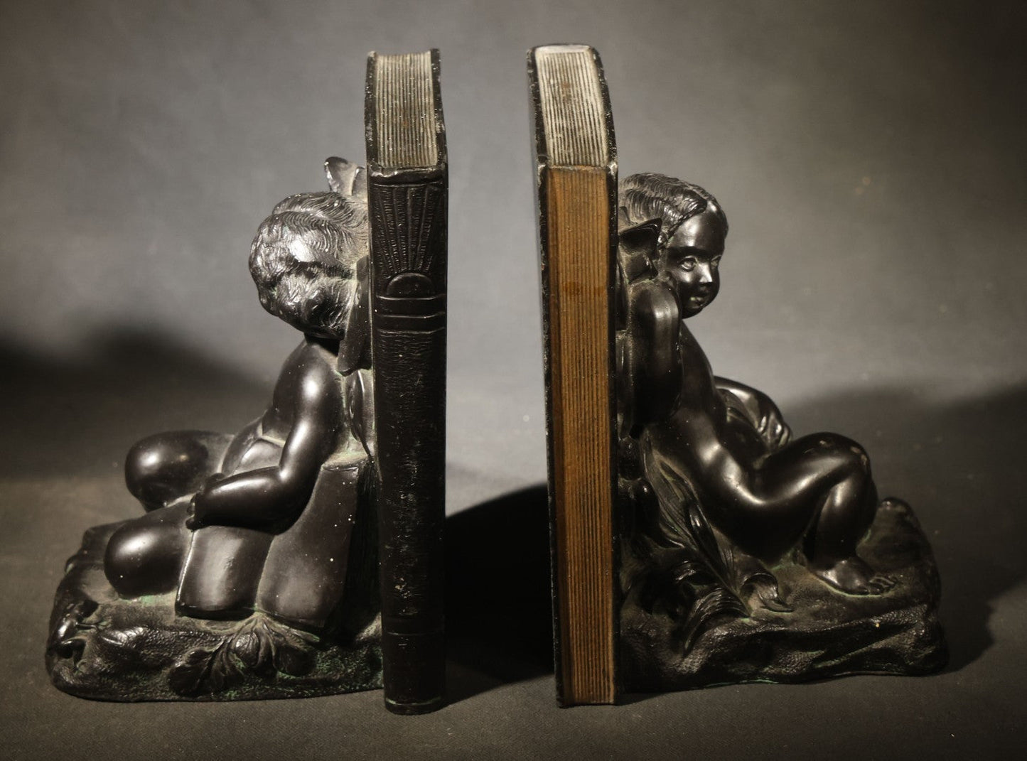 Pair of Antique Figural Bookends with Butterfly-Winged Child Seated Against Book-Form Back