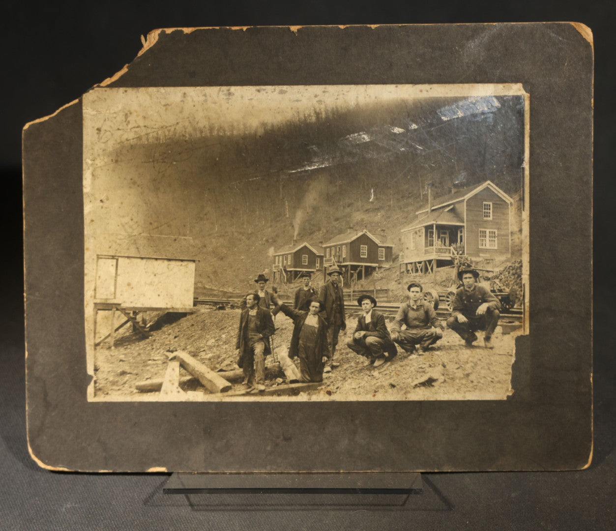 Antique Board-Mounted Occupational Photograph of Eight Railroad Workers Posed Over Railroad Ties at a Hillside Camp with Frame Buildings
