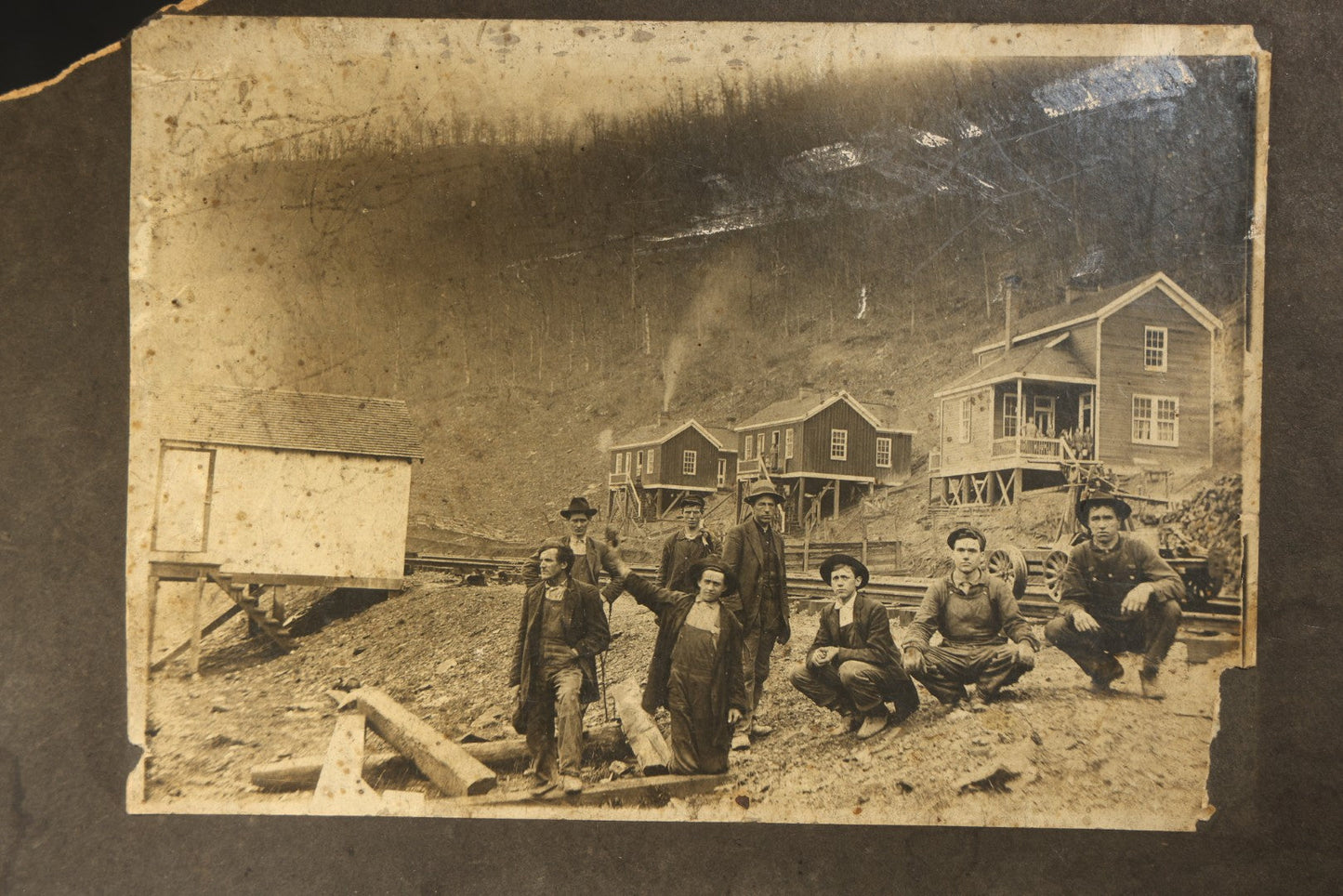 Antique Board-Mounted Occupational Photograph of Eight Railroad Workers Posed Over Railroad Ties at a Hillside Camp with Frame Buildings