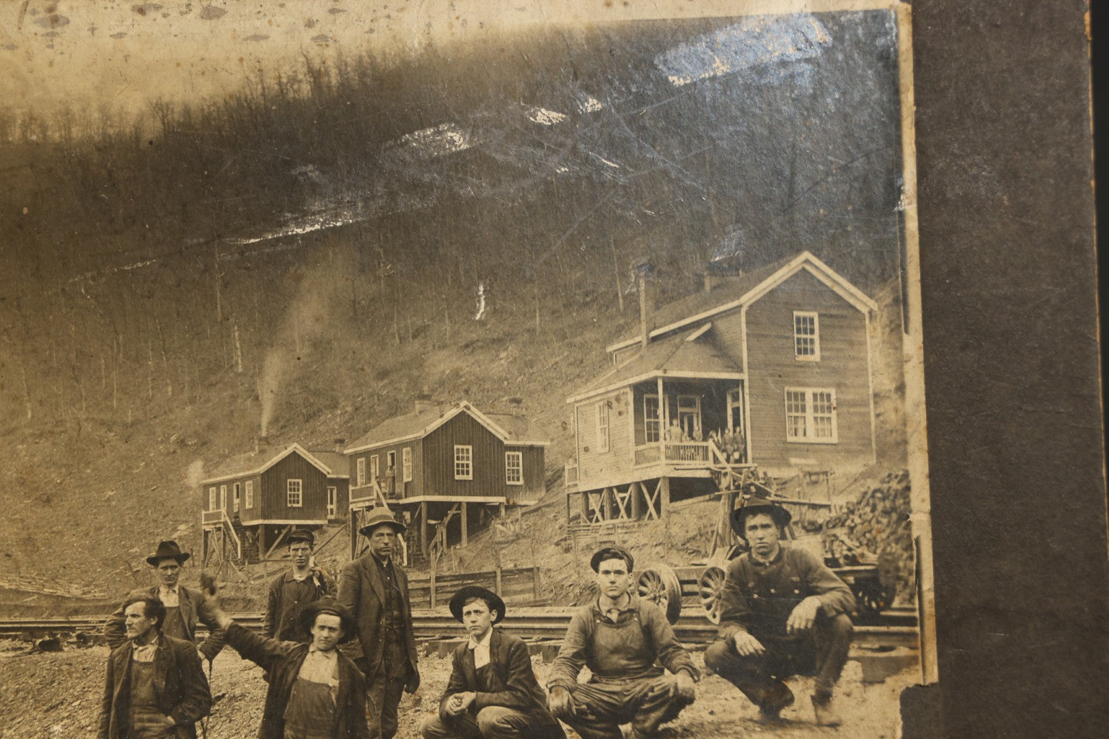 Antique Board-Mounted Occupational Photograph of Eight Railroad Workers Posed Over Railroad Ties at a Hillside Camp with Frame Buildings