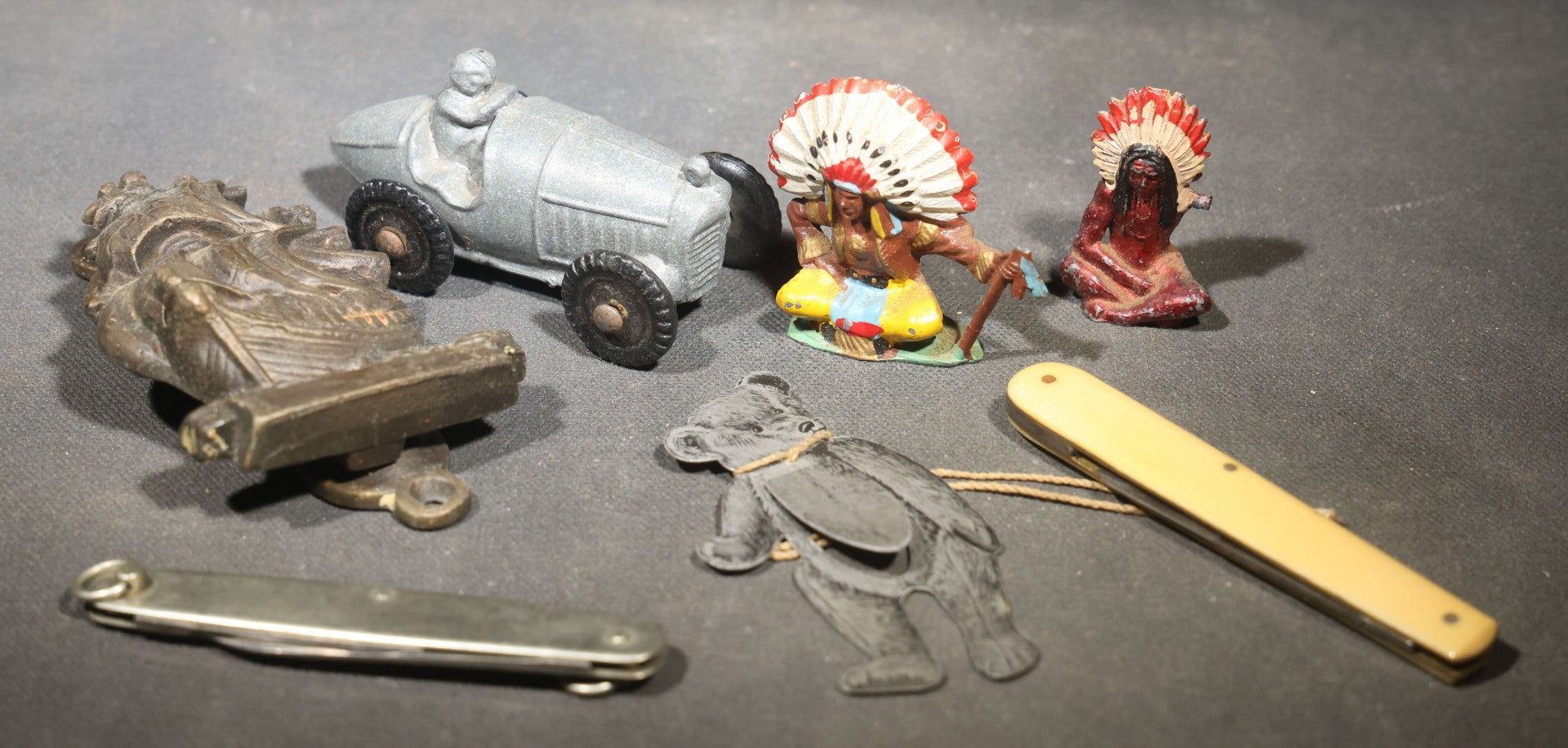 Grouping of Seven Vintage Smalls including Cast Metal Sailing Ship Door Knocker, Toy Race Car with Driver, Two Painted Native American Chief Figures, Two Pocket Knives, and Bear Bookmark
