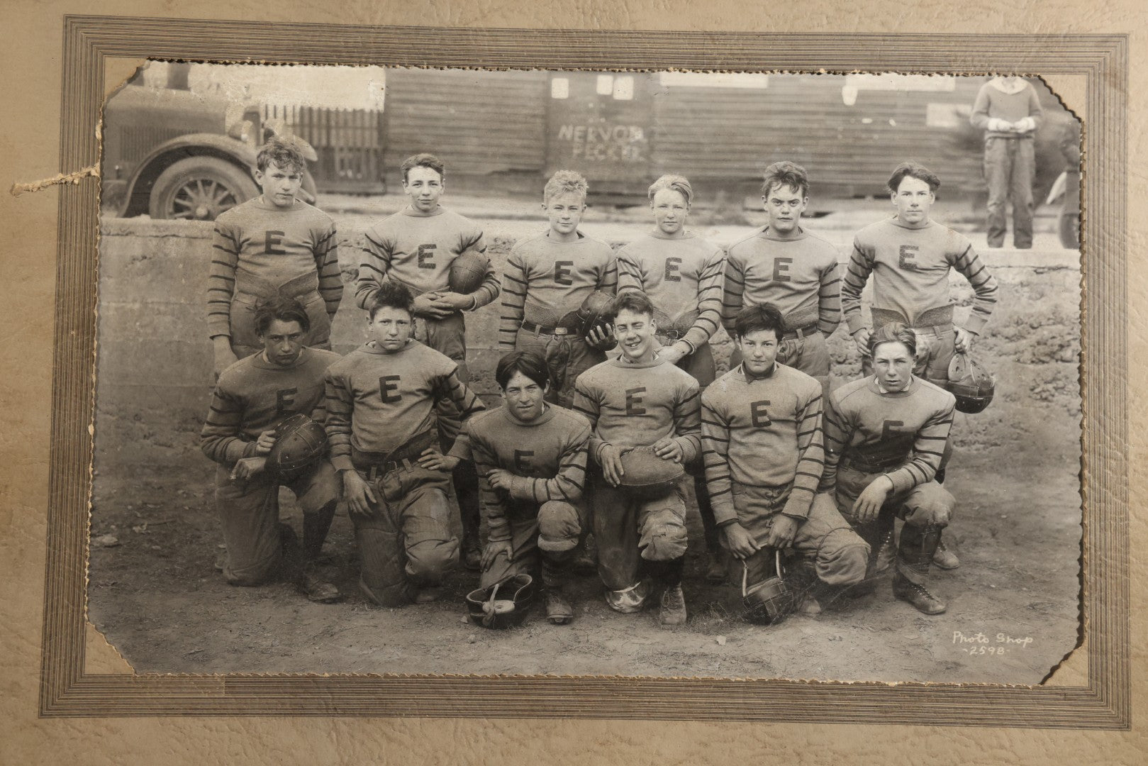 Antique Board-Mounted Photograph of a Football Team in "E" Letter Jerseys with Striped Sleeves, 12 Players with Leather Helmets and Footballs, Photographed by Photo Shop, Butte, Montana, Circa 1920s