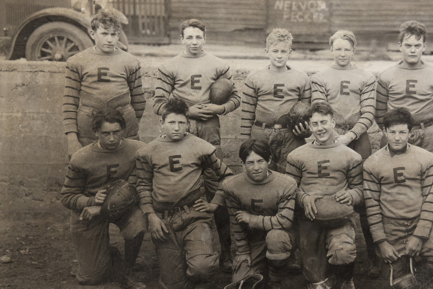 Antique Board-Mounted Photograph of a Football Team in "E" Letter Jerseys with Striped Sleeves, 12 Players with Leather Helmets and Footballs, Photographed by Photo Shop, Butte, Montana, Circa 1920s