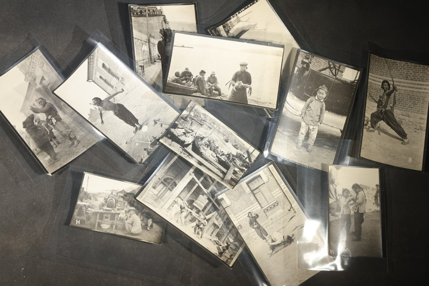 Grouping of 12 Antique Snapshot Photographs, East Asian and Russian-Language Settings including Sword Performer, Street Performer with Knife, Man with Trained Bear, Fishermen with Crabs, Construction Workers, and Children