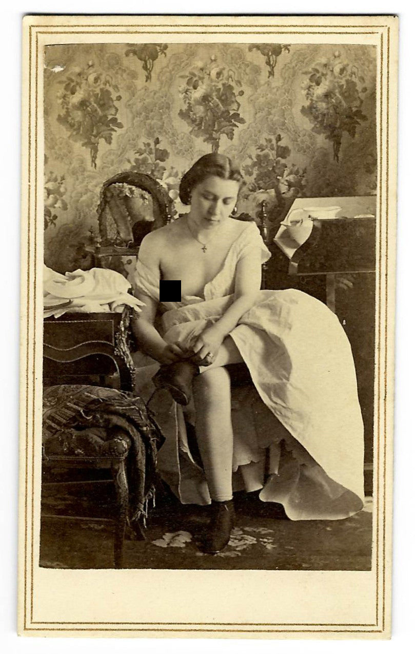 Antique Risque Carte de Visite C.D.V. Photograph of a Partially Nude Woman Seated on a Bed with Exposed Breast, Wearing a Cross Necklace and Stockings