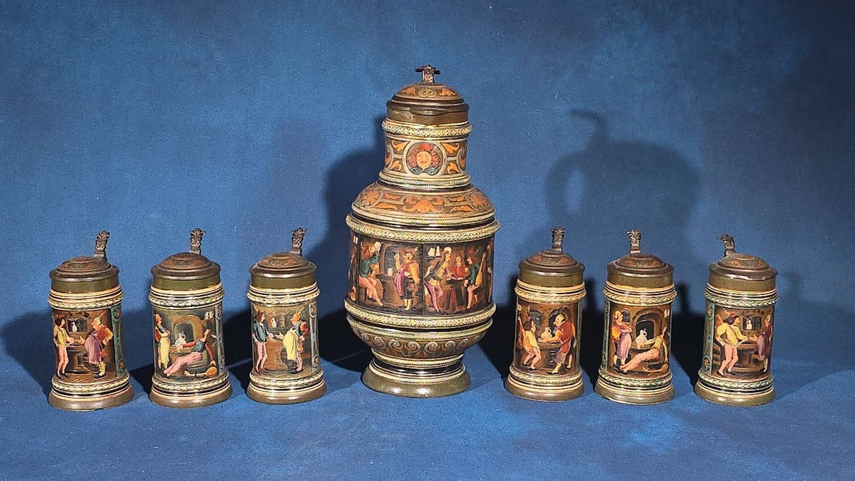 Grouping of Six Antique German Pottery Steins and Lidded Pitcher with Tavern Scenes, Stamped Germany