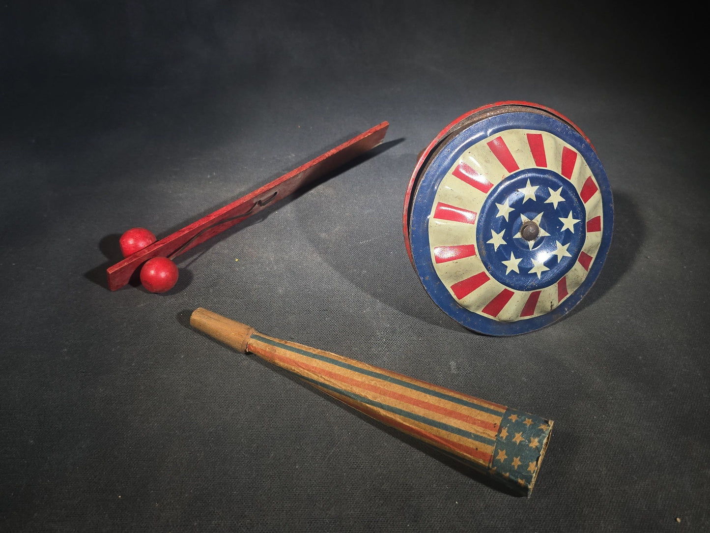 Trio of Antique Patriotic Noisemakers including Tin Lithograph Noisemaker with Stars and Stripes, Paper Horn, and Red Wooden Ball Clapper