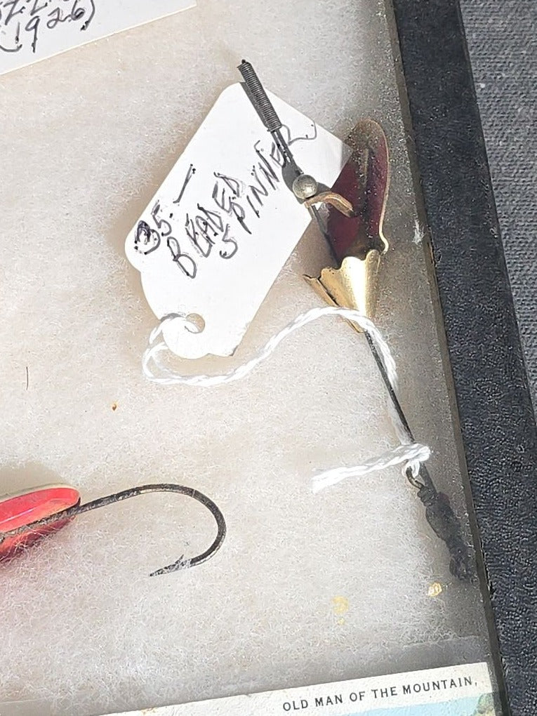 Grouping of Antique and Vintage Fishing Lures in Riker Display Case including Jazz Wiggler, Oriental Wiggler, Bladed Spinner, and South Bend, with Old Man of the Mountain Postcard