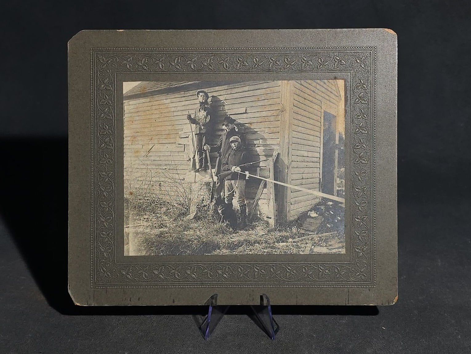 Antique Board-Mounted "Selfie" Photograph of Three Hunters with Rifles and Game Posed Outside a Wooden Building, Self-Timed Shutter Release