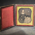 Lot 018 - Antique 1/6th Plate Daguerreotype Photograph of a Child Standing Beside a Cloth-Covered Table with a Cap in Full Intact Leatherette Union Case with Embossed Floral and Scroll Design