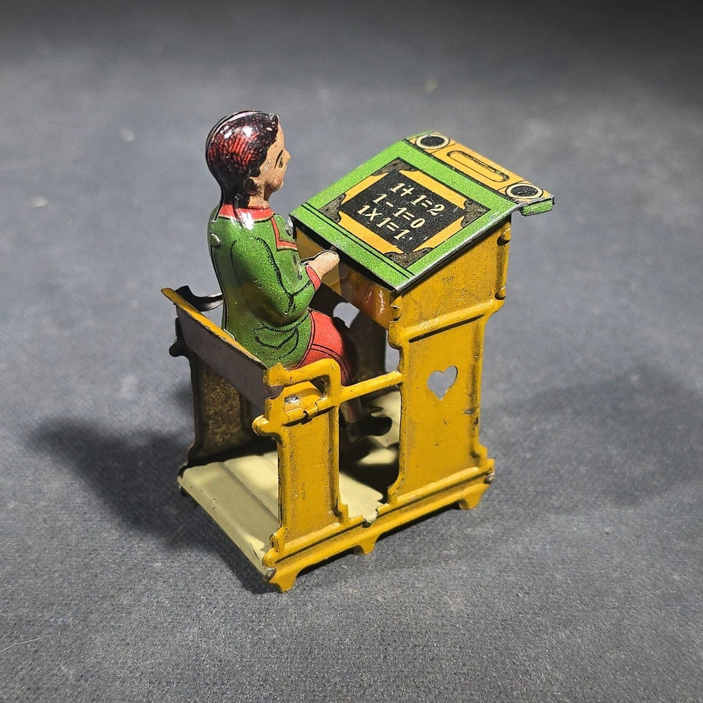 Grouping of Four Antique and Vintage Tin Lithograph Miniature Toys including Student at Desk, Two Miniature Travel Suitcases with Hotel and Travel Labels, and Pair of Seated Figures in Helmets