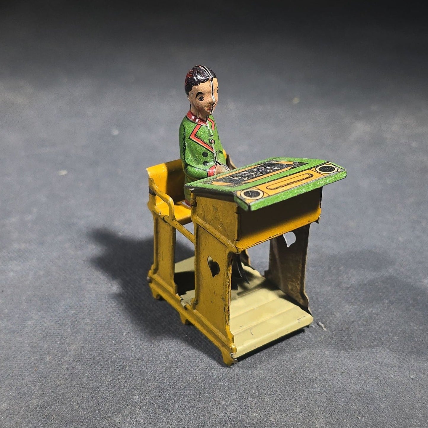 Grouping of Four Antique and Vintage Tin Lithograph Miniature Toys including Student at Desk, Two Miniature Travel Suitcases with Hotel and Travel Labels, and Pair of Seated Figures in Helmets