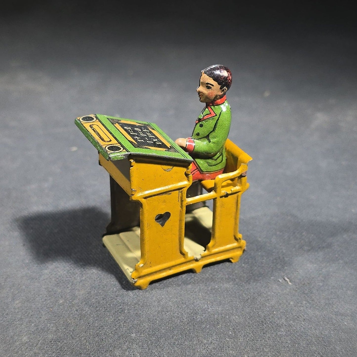 Grouping of Four Antique and Vintage Tin Lithograph Miniature Toys including Student at Desk, Two Miniature Travel Suitcases with Hotel and Travel Labels, and Pair of Seated Figures in Helmets