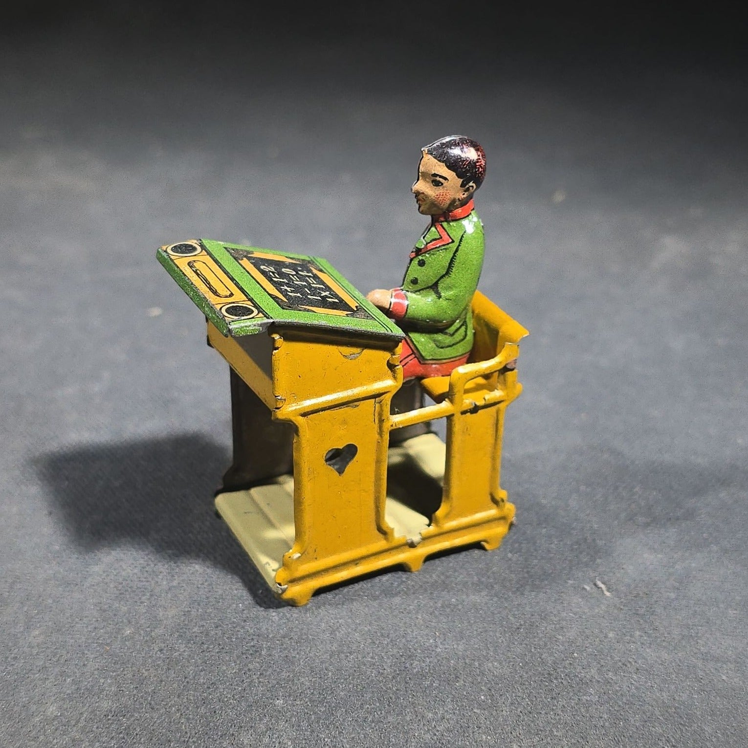 Grouping of Four Antique and Vintage Tin Lithograph Miniature Toys including Student at Desk, Two Miniature Travel Suitcases with Hotel and Travel Labels, and Pair of Seated Figures in Helmets