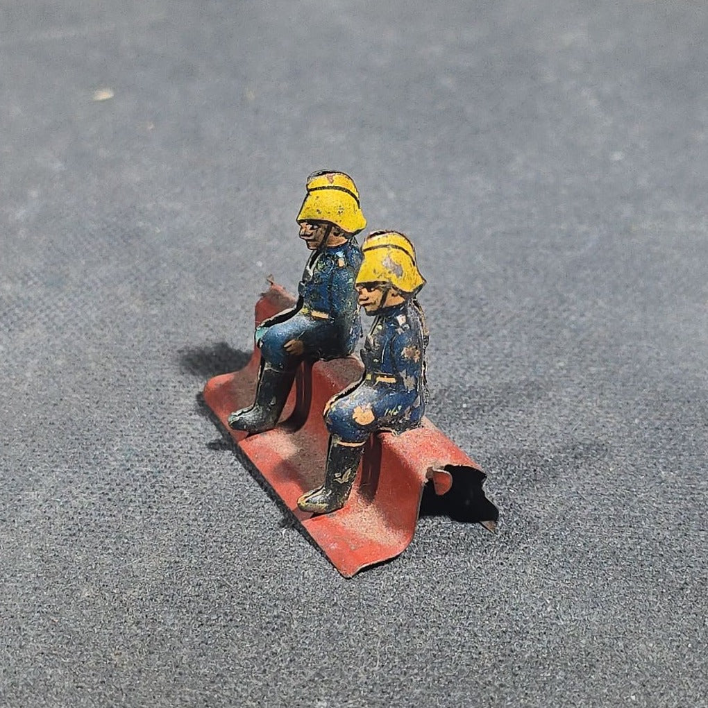 Grouping of Four Antique and Vintage Tin Lithograph Miniature Toys including Student at Desk, Two Miniature Travel Suitcases with Hotel and Travel Labels, and Pair of Seated Figures in Helmets