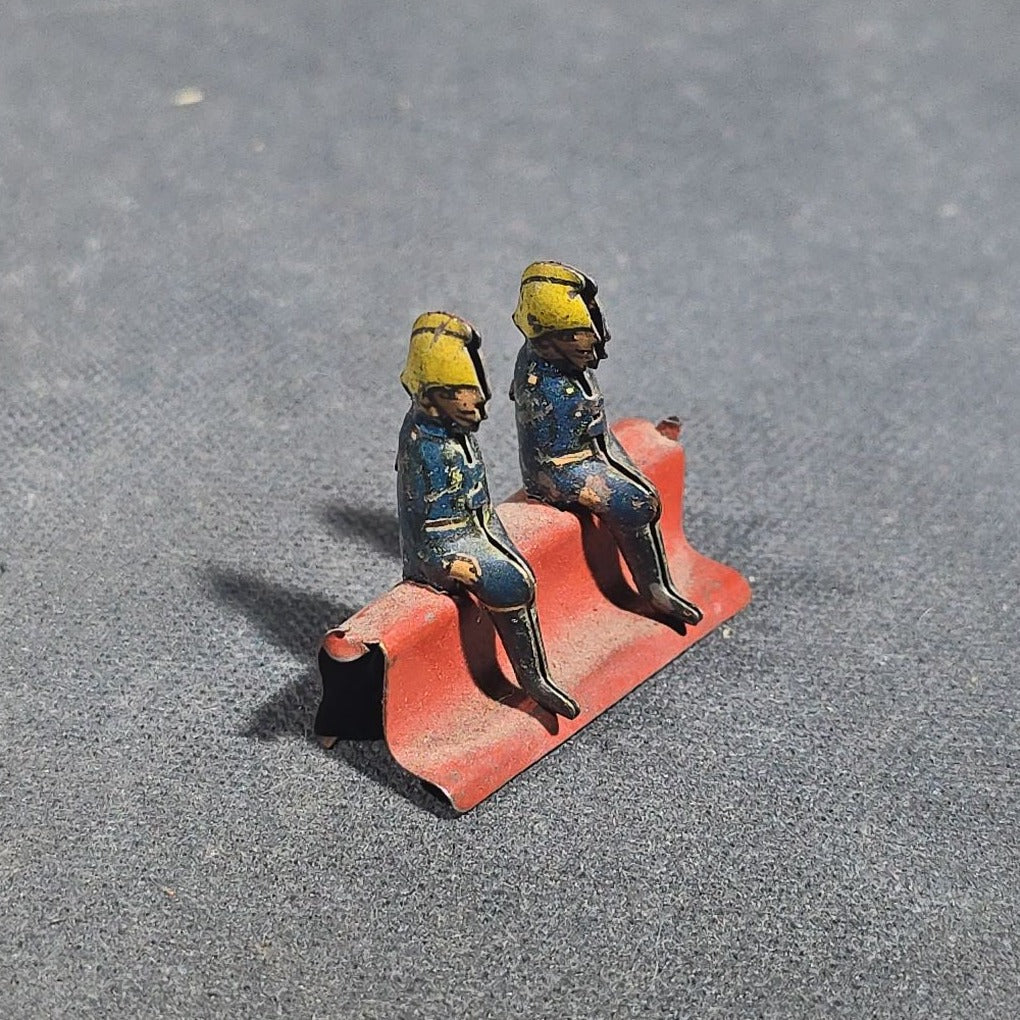 Grouping of Four Antique and Vintage Tin Lithograph Miniature Toys including Student at Desk, Two Miniature Travel Suitcases with Hotel and Travel Labels, and Pair of Seated Figures in Helmets