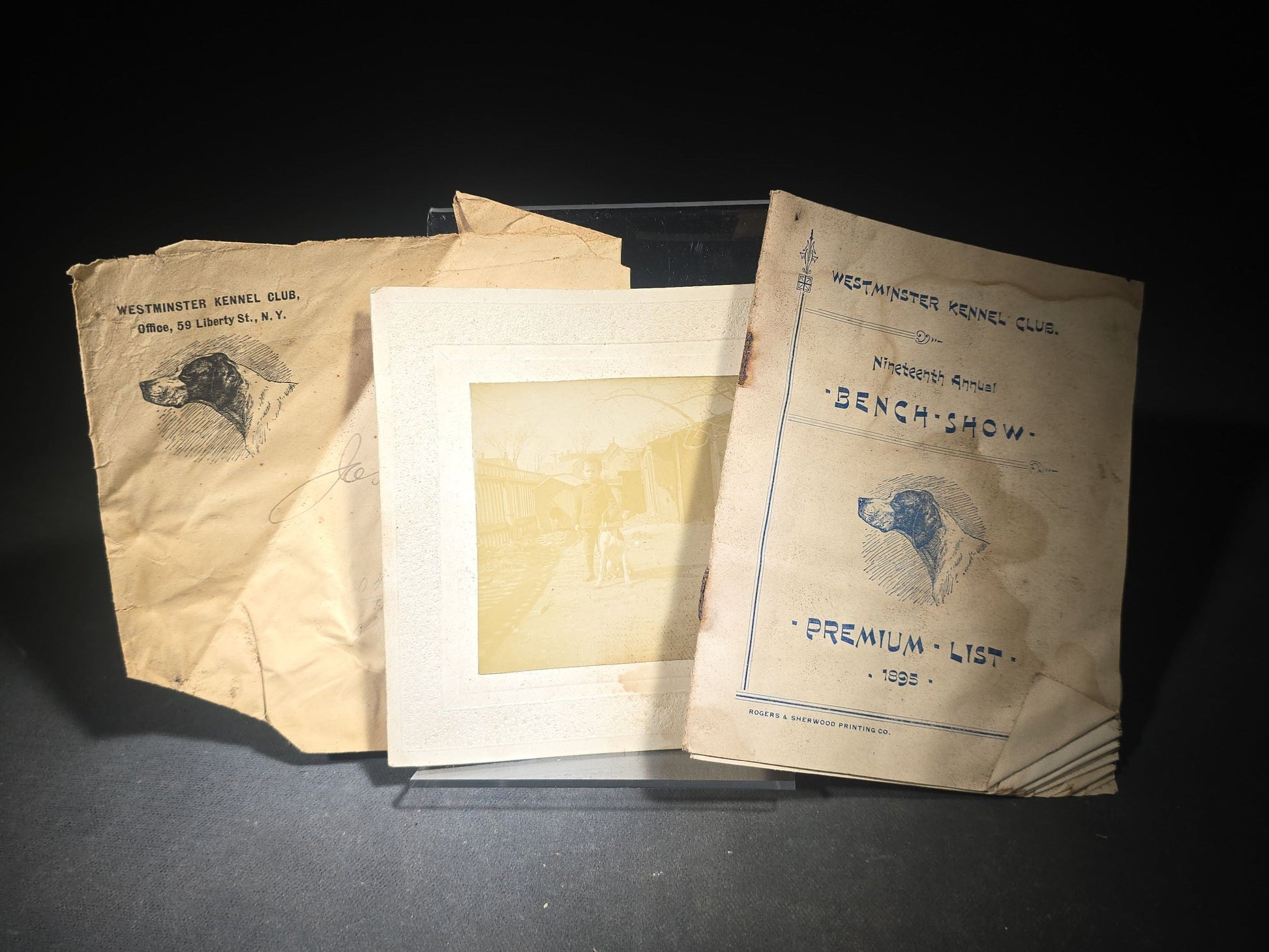 Grouping of Three Antique Westminster Kennel Club Dog Ephemera Pieces including 1895 Nineteenth Annual Bench Show Premium List with Spratts Patent Advertising, Illustrated Mailing Envelope, and Board-Mounted Photograph of a Child with a Dog